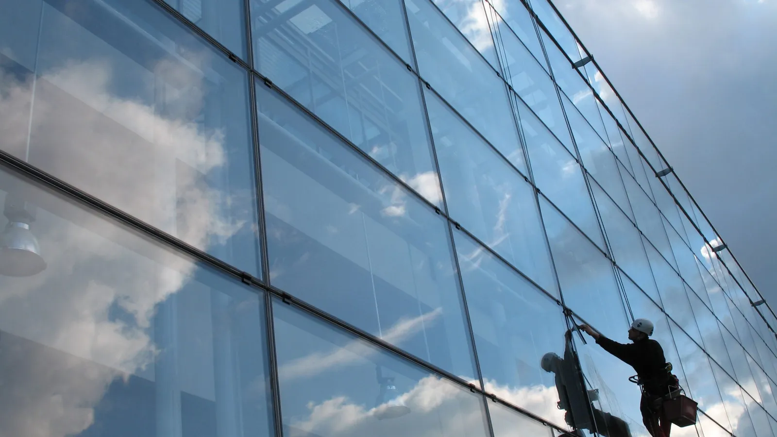 Window cleaner working on reflective glass building facade