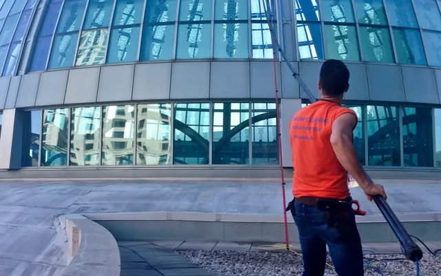 Worker cleaning glass dome building with pressure washer
