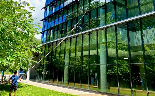 Man cleaning large glass building exterior with hose.