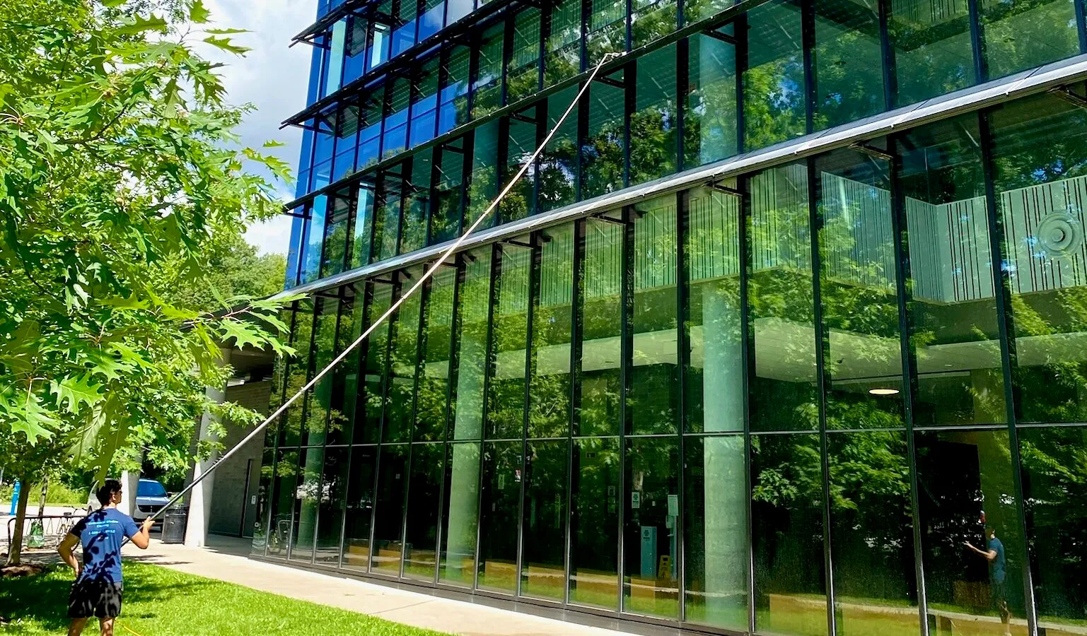 Man cleaning large glass building exterior with hose.