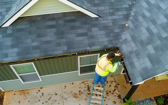 A worker is cleaning clogs in roof gutter drain by picking up dirt, debris, fallen leaves