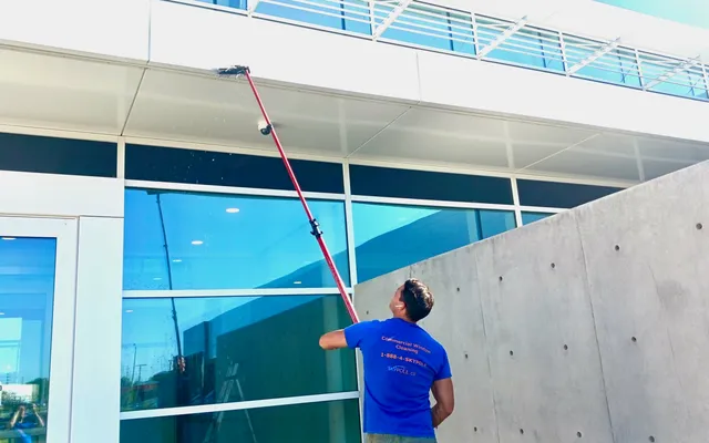 Man using long pole to clean large building exterior surface.