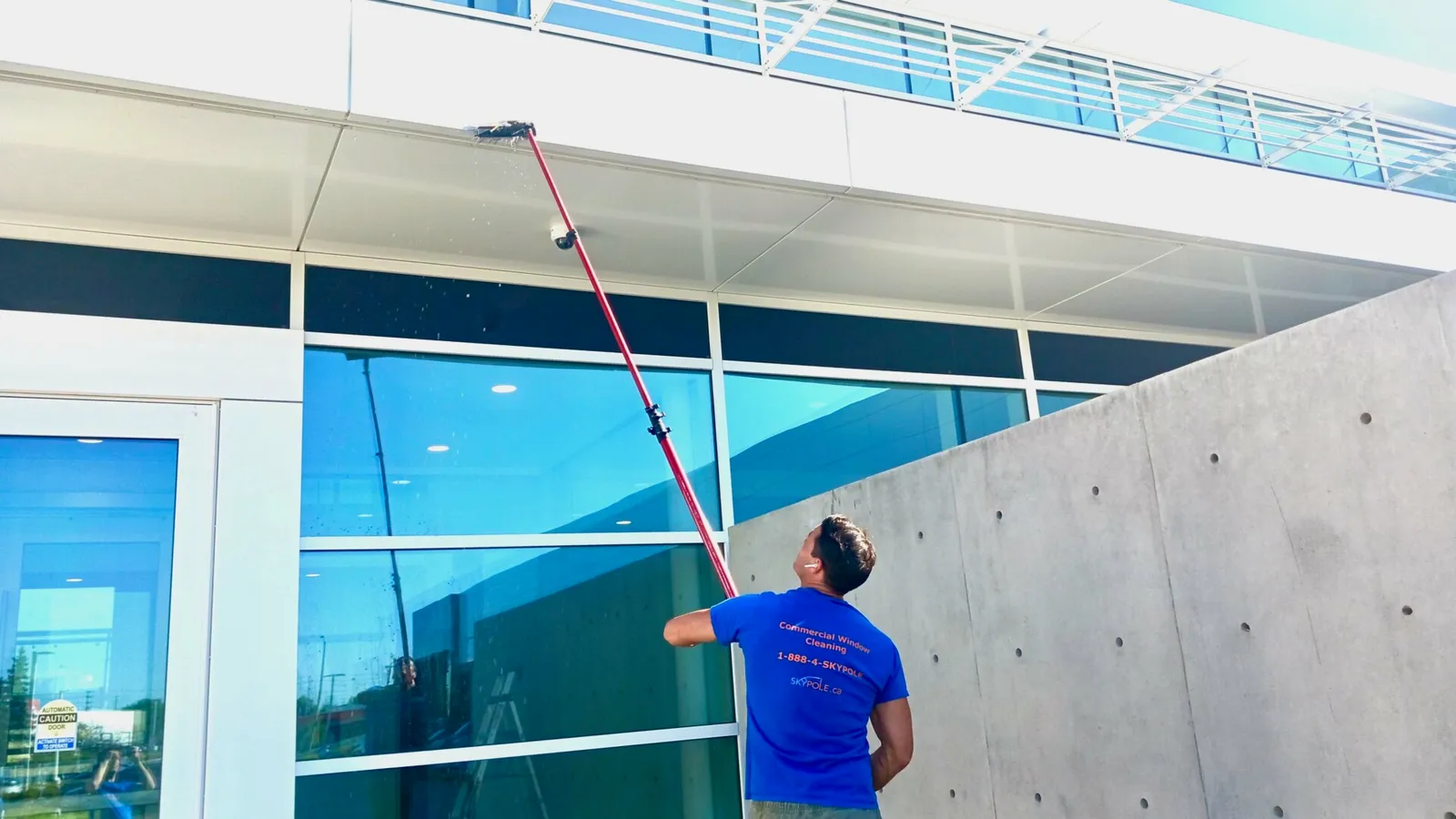 Man using long pole to clean large building exterior surface.