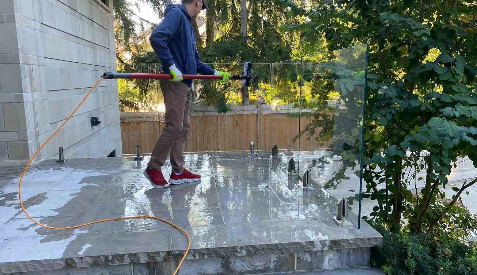 Man cleaning outdoor glass surface with water-fed pole.