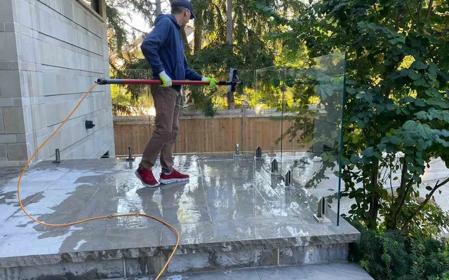 Man cleaning outdoor glass surface with water-fed pole.