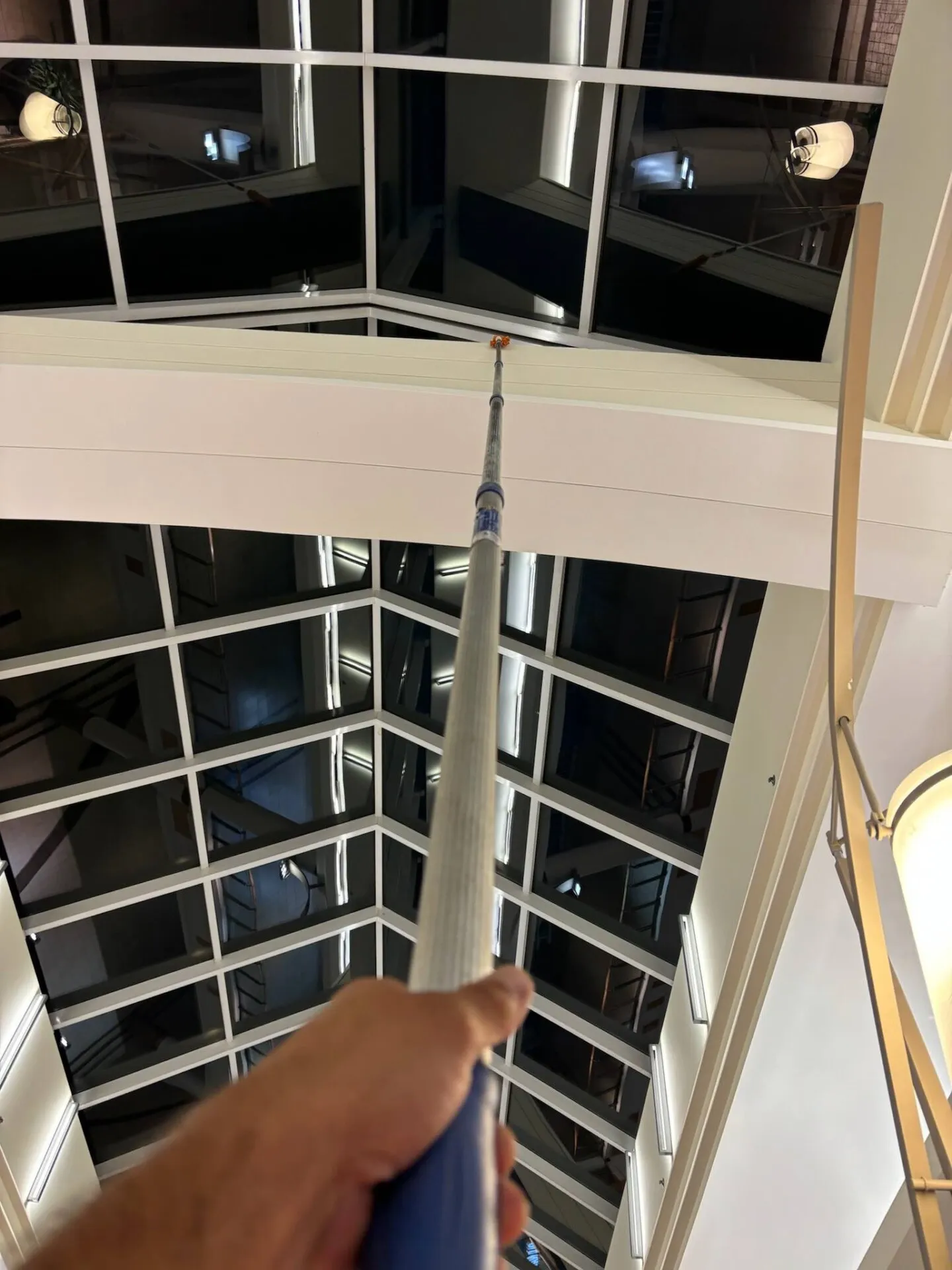 Hand holding pole reaching overhead light fixture to clean it