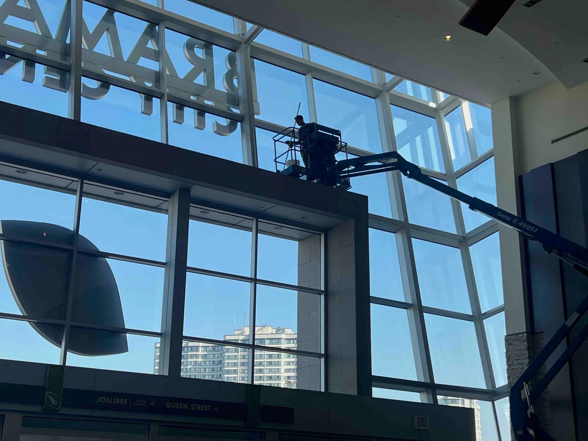 Worker on lift cleaning large glass windows indoors