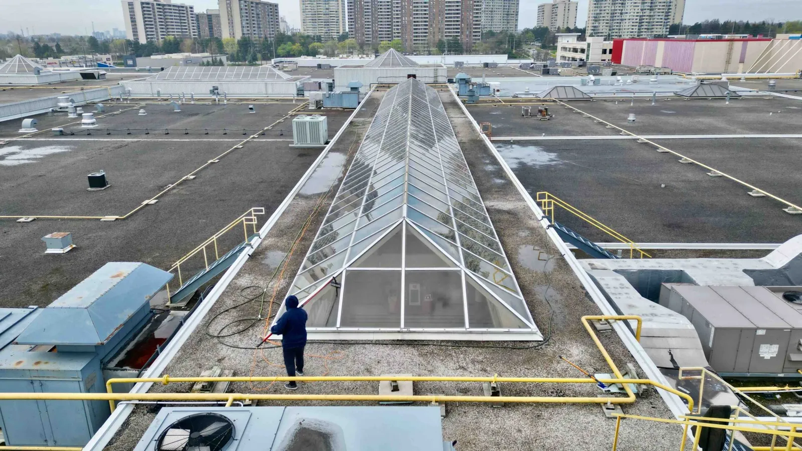 Worker cleaning rooftop skylight amidst urban buildings