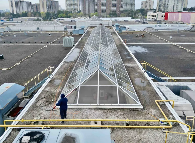 Worker cleaning rooftop skylight amidst urban buildings
