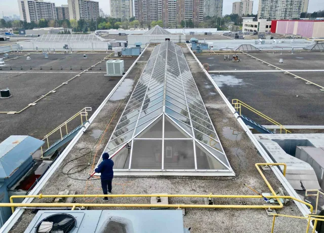 Worker cleaning rooftop skylight amidst urban buildings