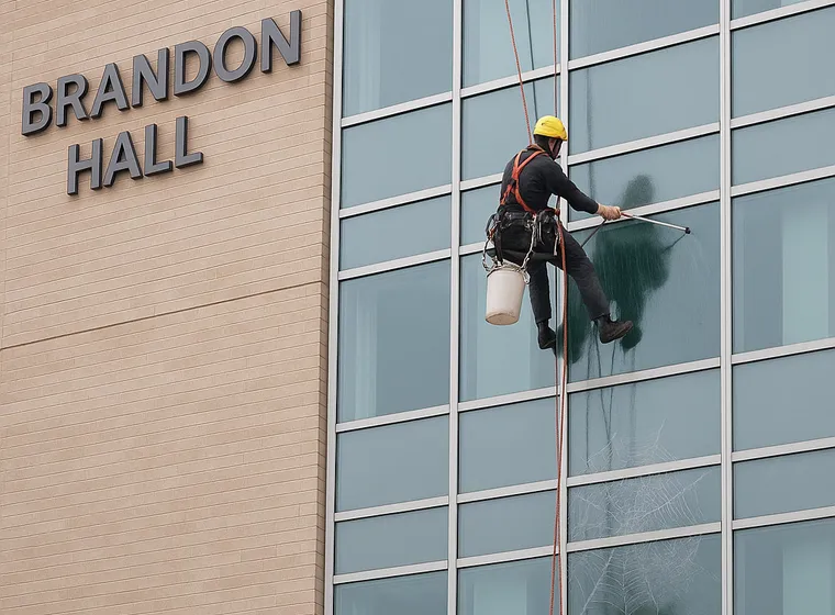Worker cleaning windows on Brandon Hall building