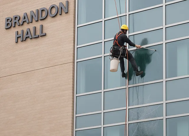 Worker cleaning windows on Brandon Hall building