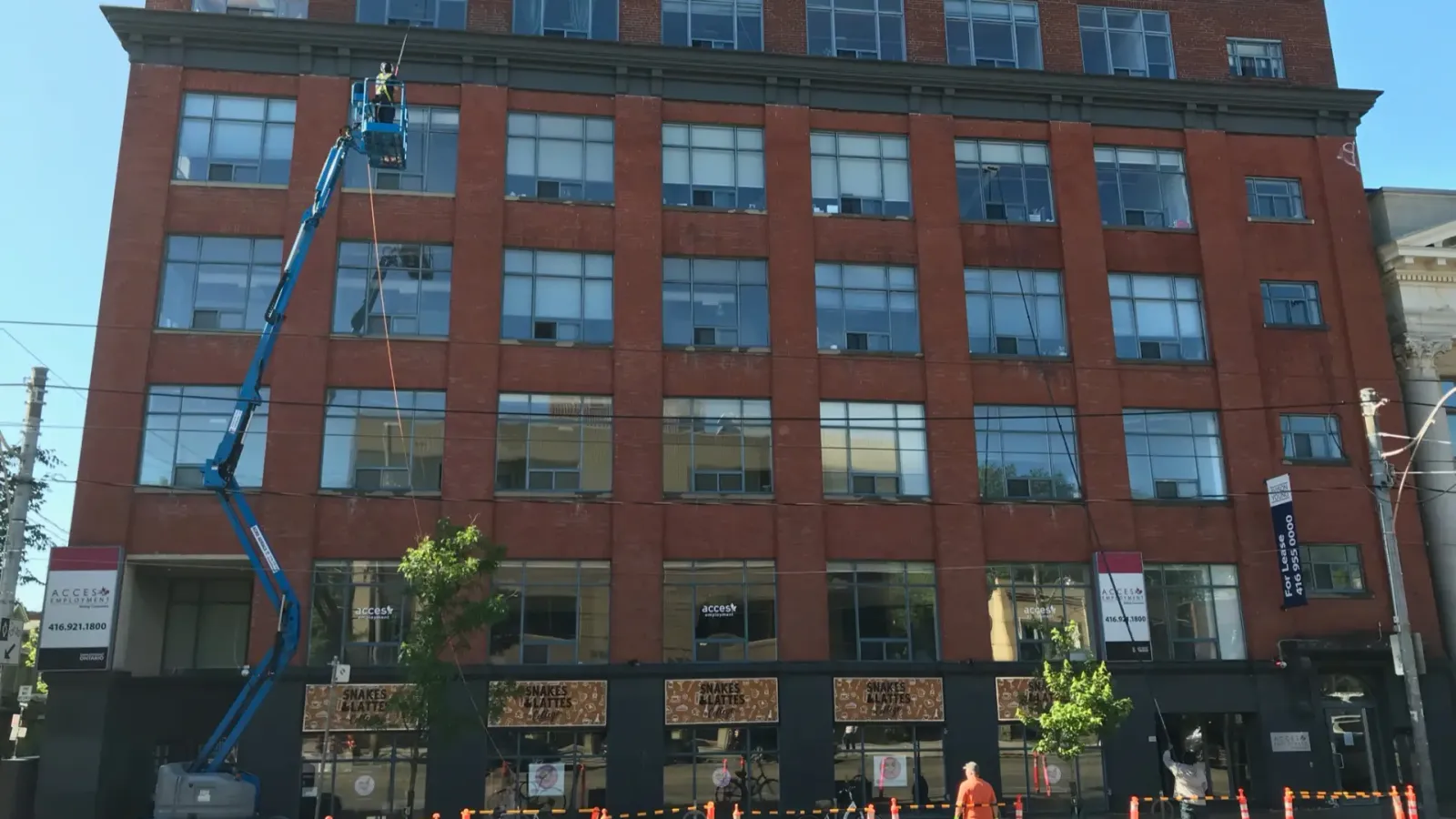 Worker on articulated boom lift cleaning windows on red building.