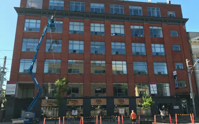 Worker on articulated boom lift cleaning windows on red building.