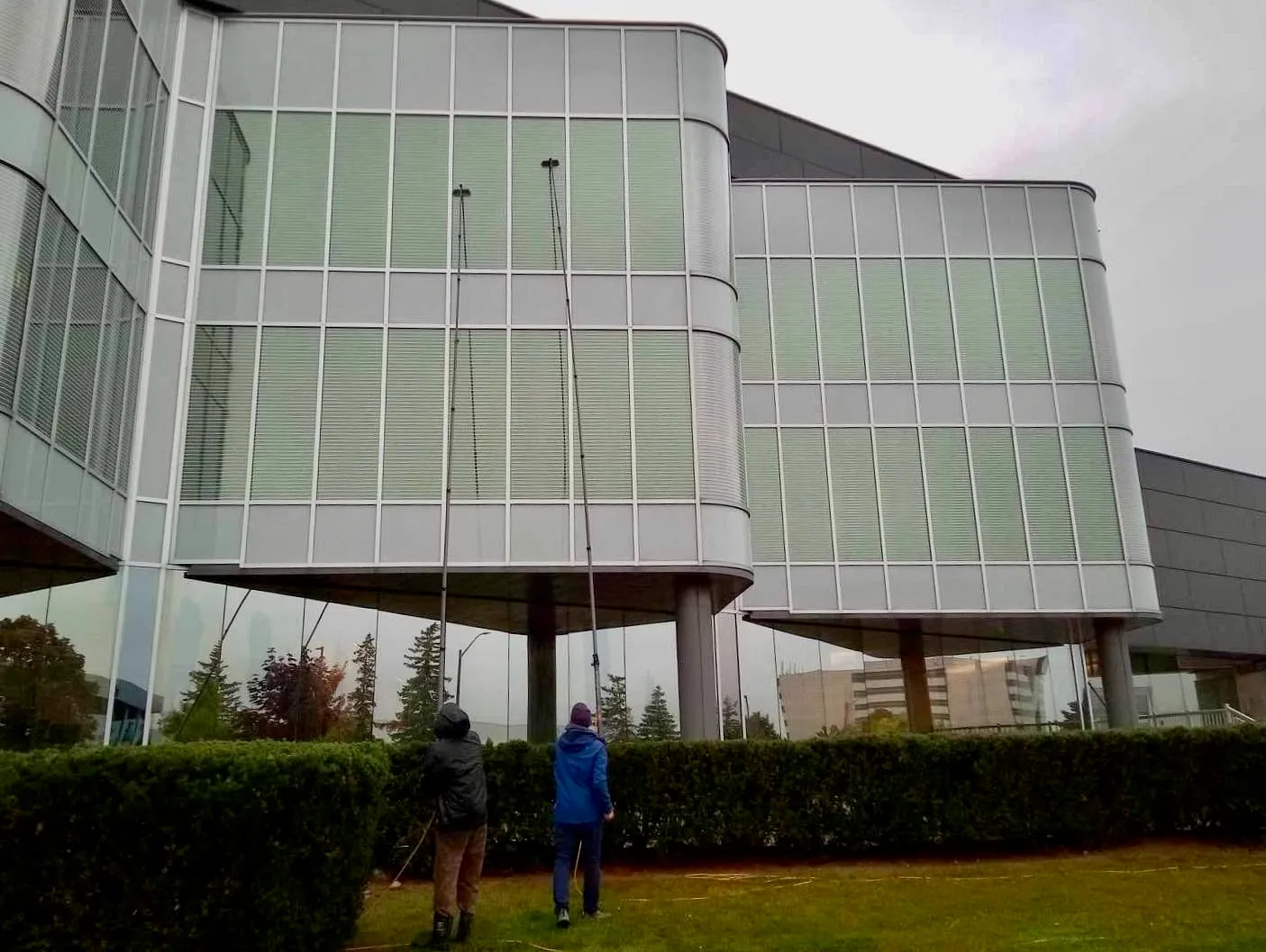 Two people cleaning the windows of a large modern glass building