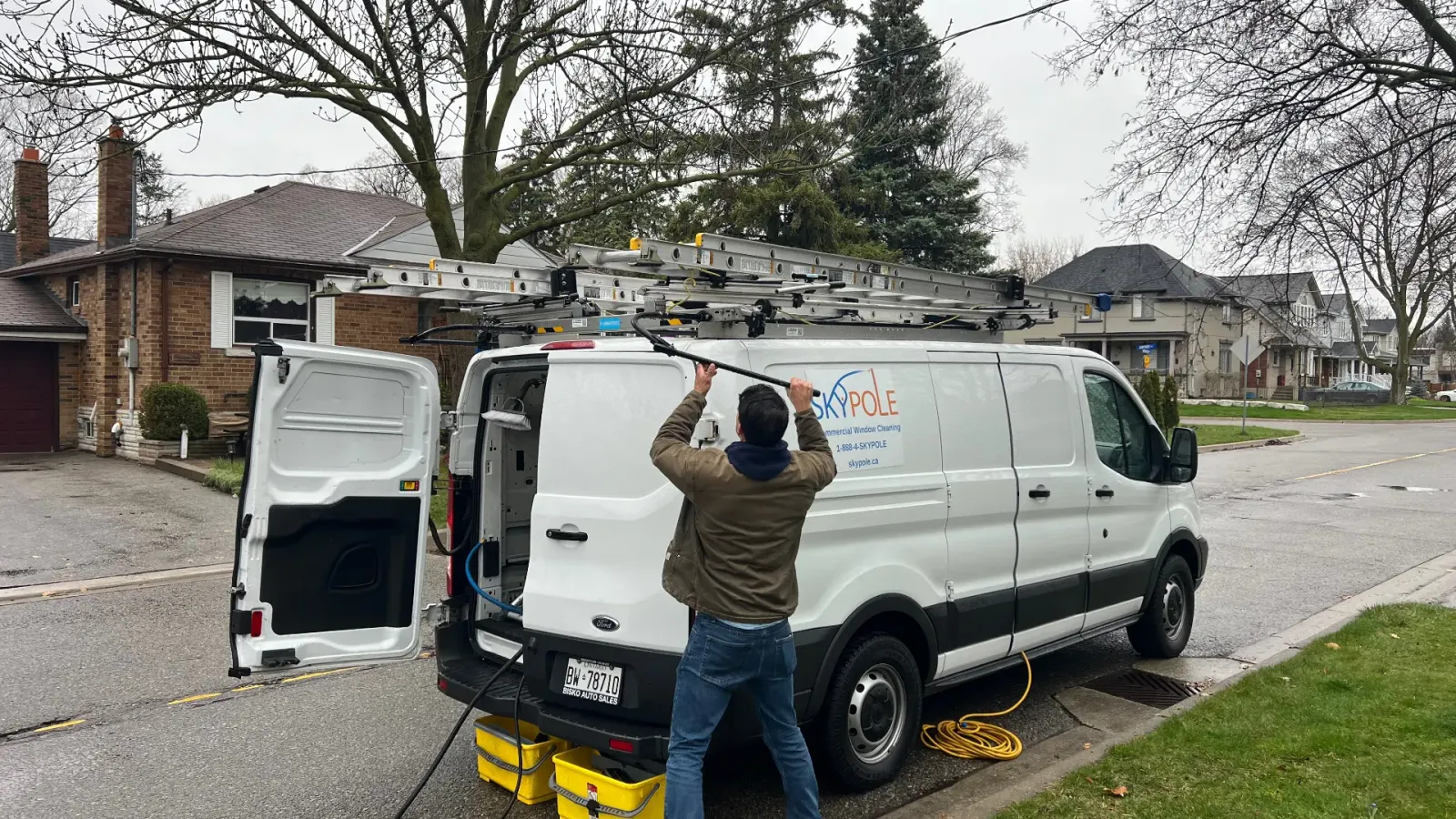 Man loading equipment onto roof of van in driveway.