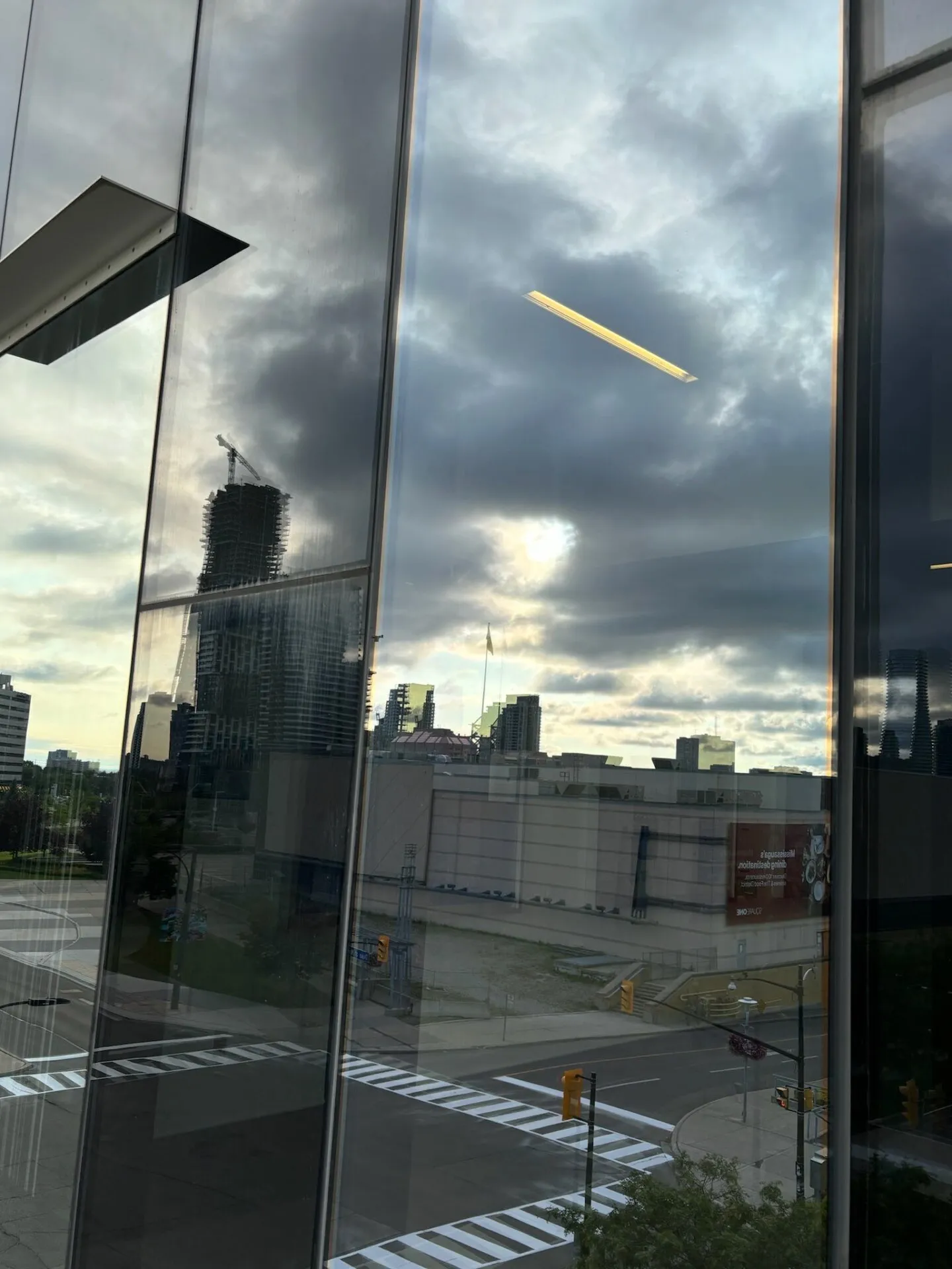 Urban skyline reflected on glass building under cloudy sky