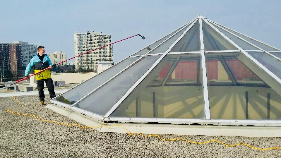 Worker cleaning a glass pyramid rooftop with hose