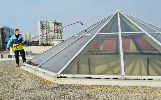 Worker cleaning a glass pyramid rooftop with hose