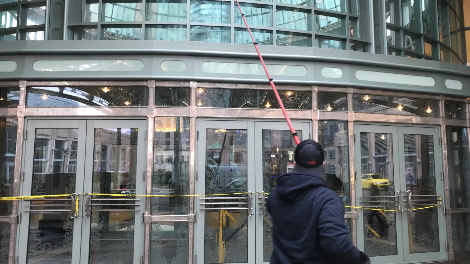 Worker cleaning glass building entrance with long tool