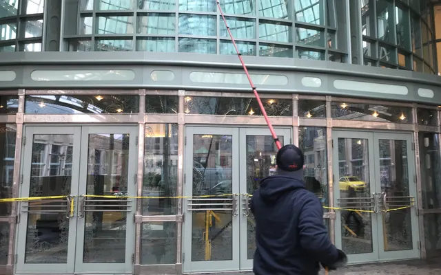 Worker cleaning glass building entrance with long tool