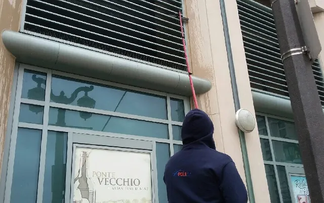 Person cleaning building facade with telescopic pole