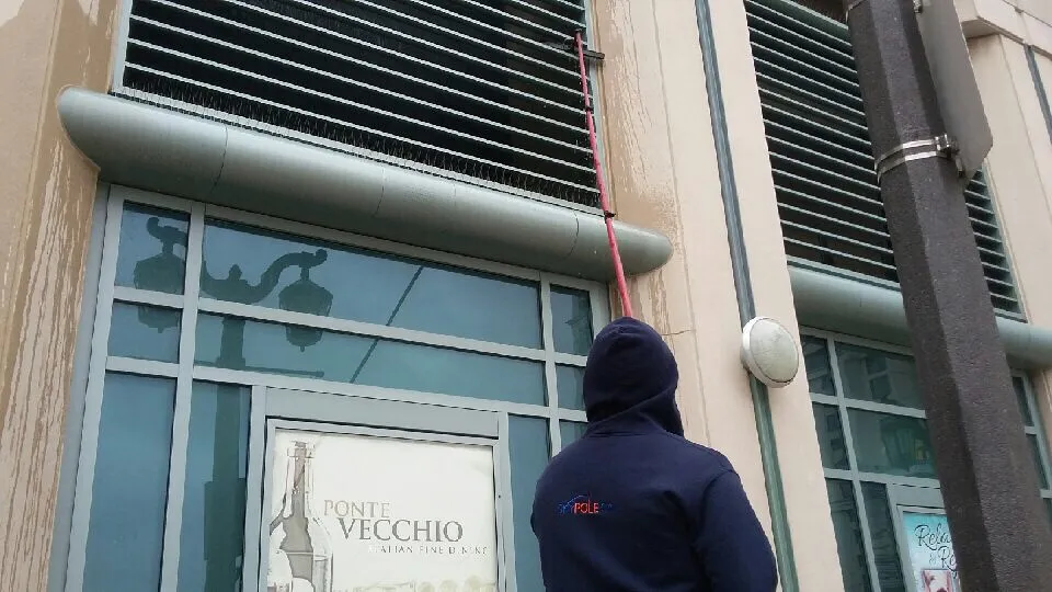 Worker cleaning building facade and metal louvres with water fed pole