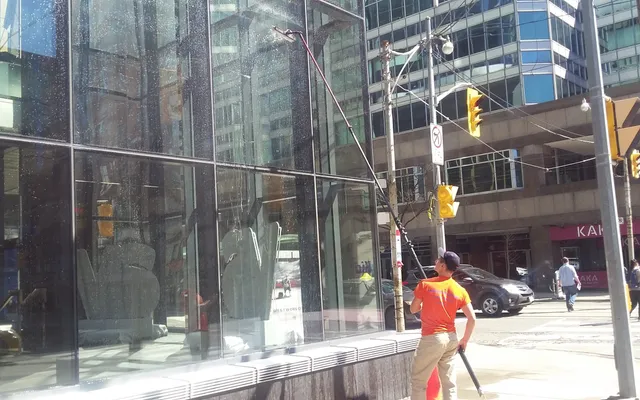 Worker cleaning glass building facade on sunny day