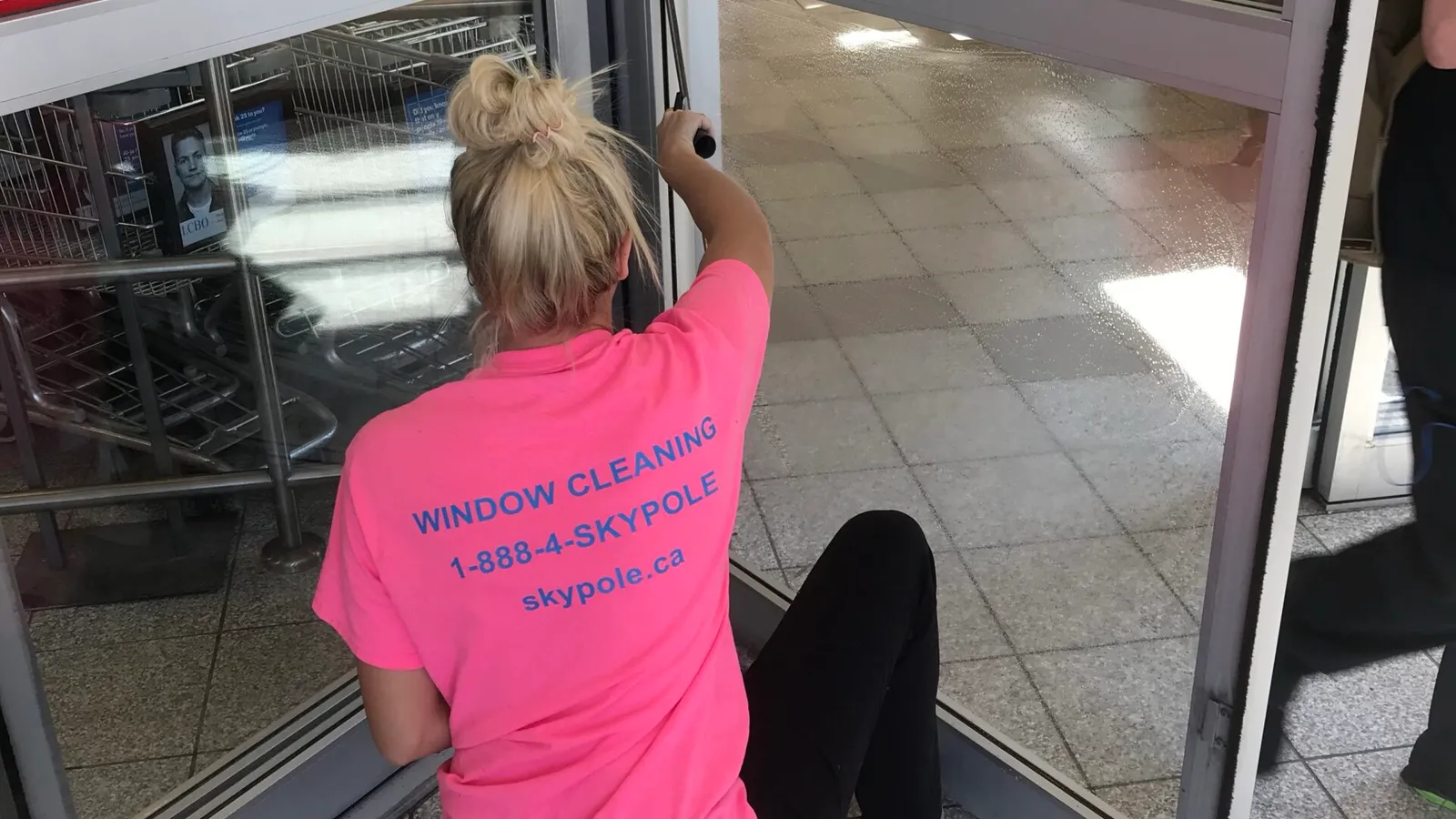Worker in pink shirt cleaning automatic sliding door