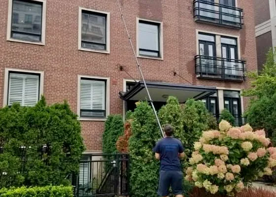Man cleaning windows with long pole outside brick building.