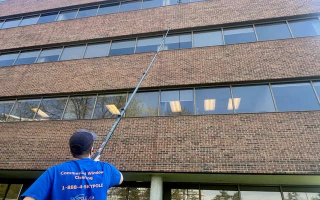 Man cleaning office windows with long pole.