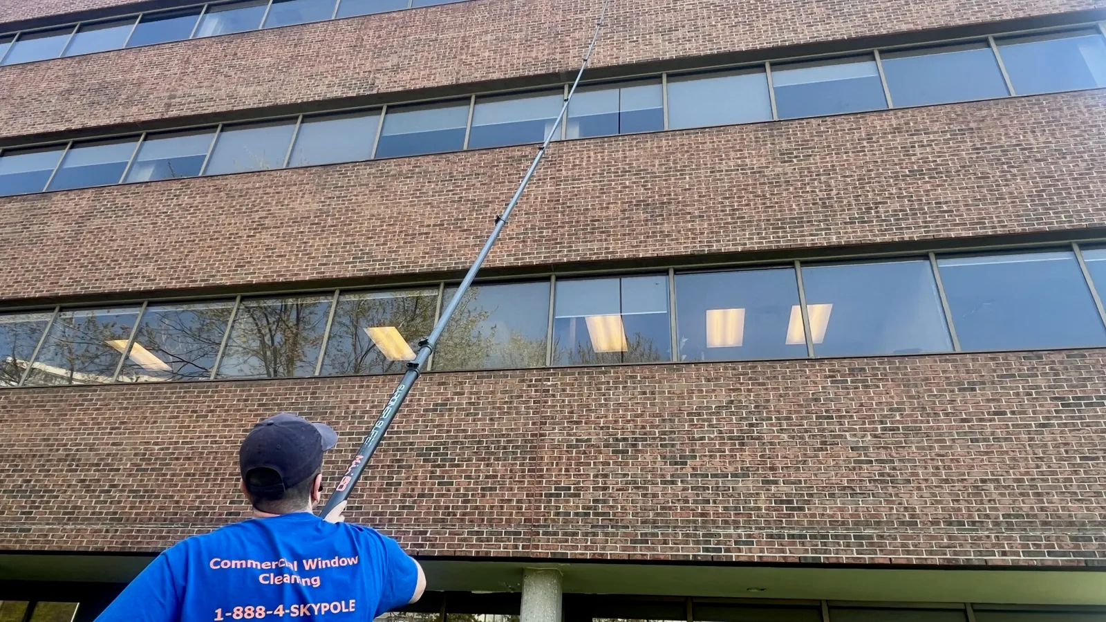 Man cleaning office windows with long pole.