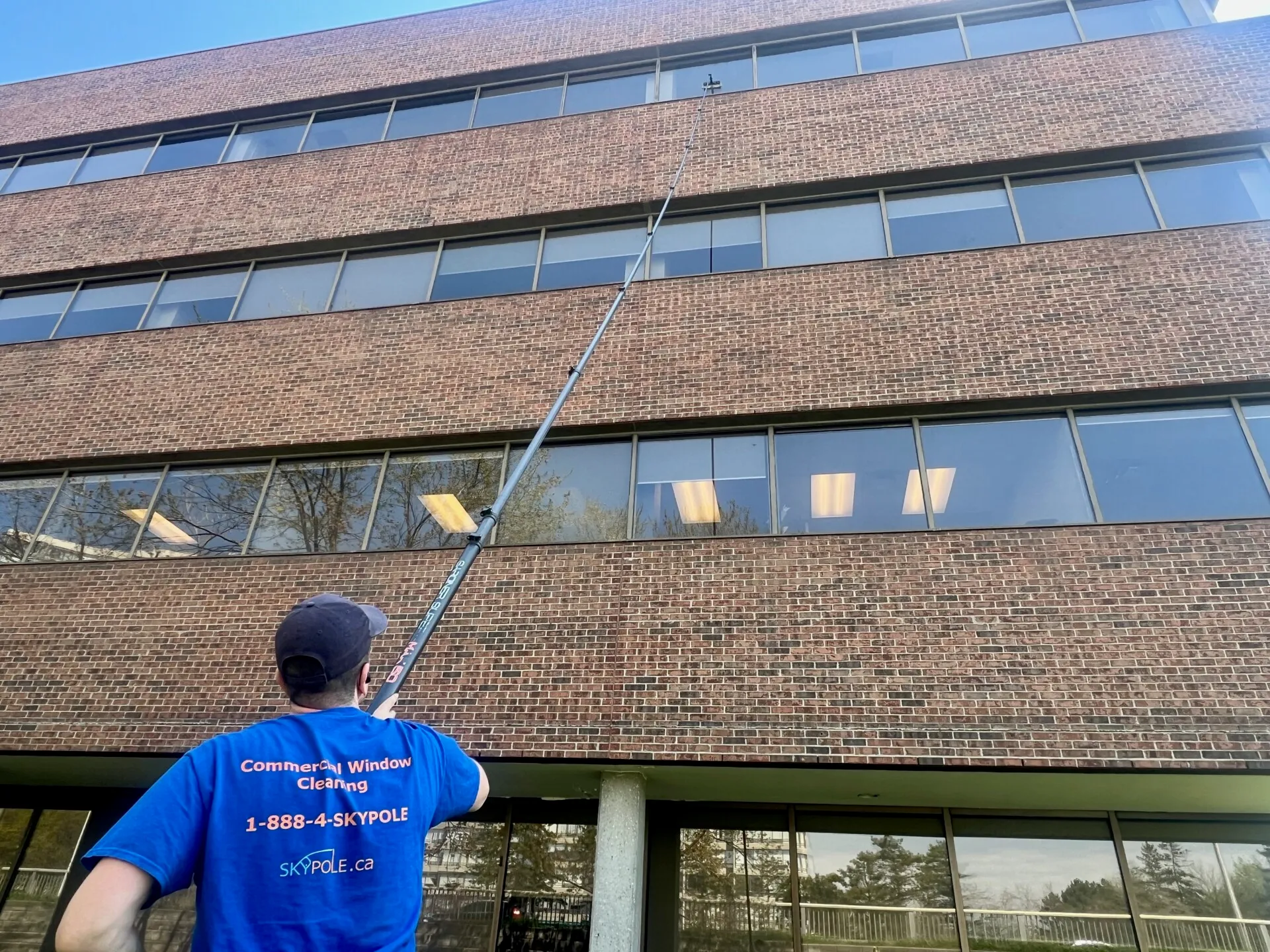 Man cleaning office windows with long pole.
