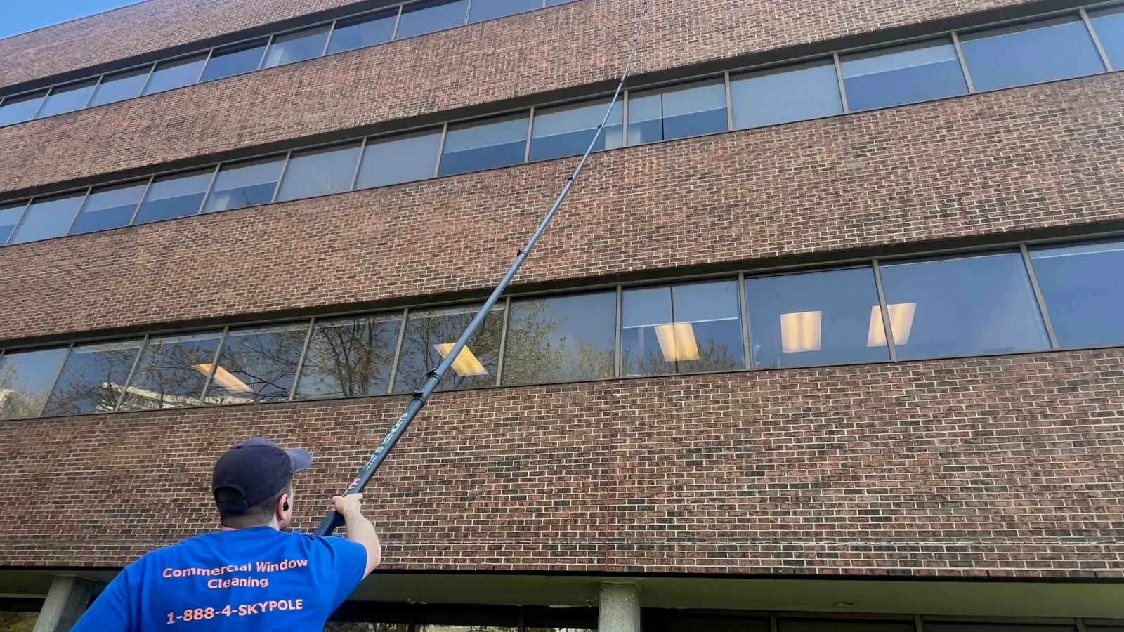 Window cleaner using telescopic pole at office building.