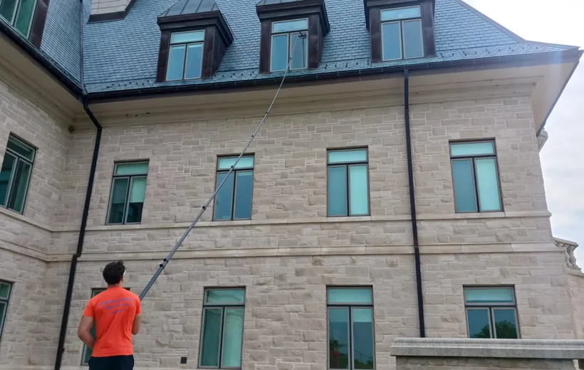 Man cleaning large stone house using long-handled brush