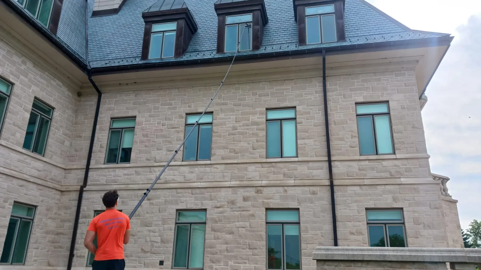 Man cleaning large stone house using long-handled brush