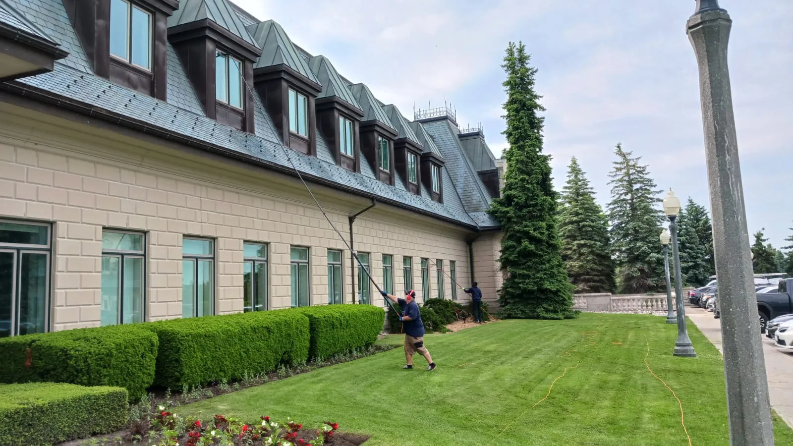 Workers cleaning mansion windows with long-handled brushes