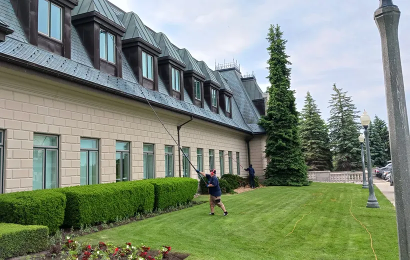 Workers cleaning mansion windows with long-handled brushes