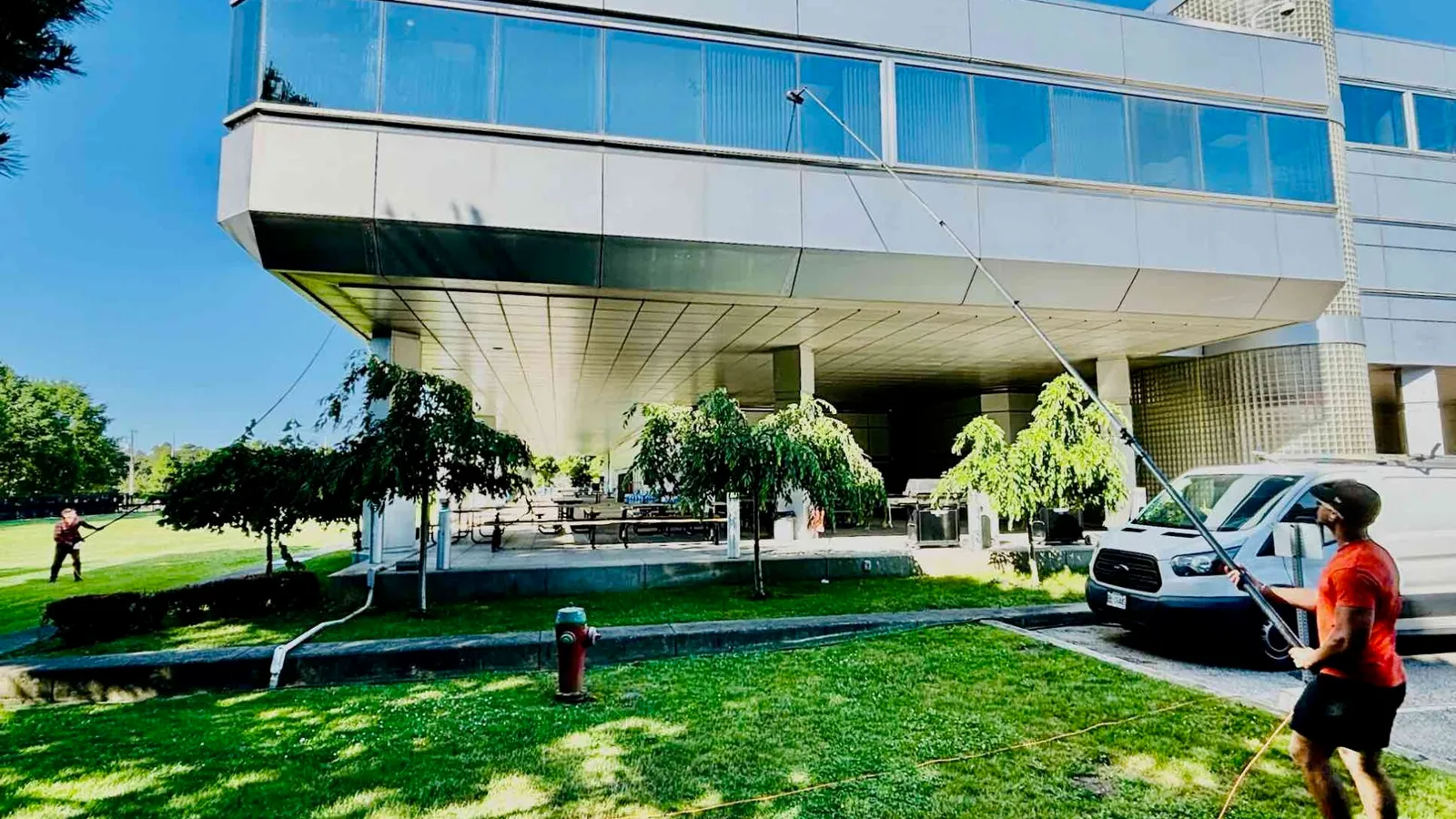 Man power washing modern building exterior on sunny day