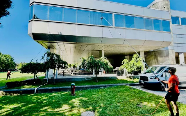 Man power washing modern building exterior on sunny day