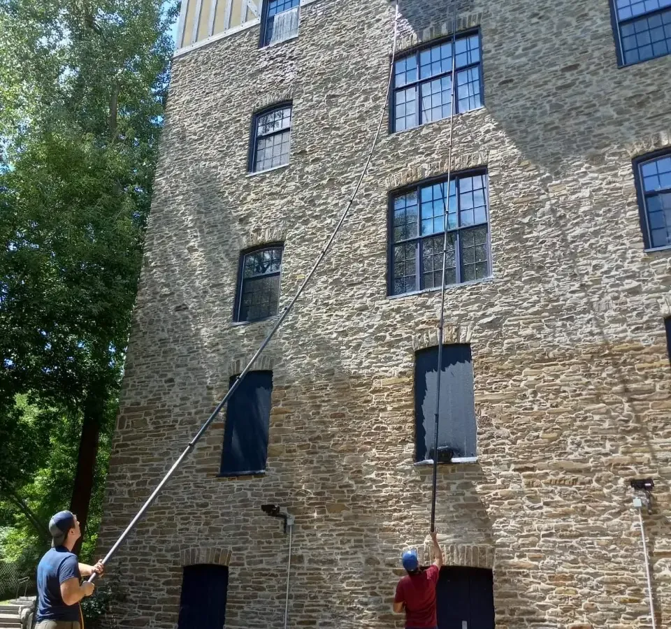 Two men cleaning windows of a large stone building.