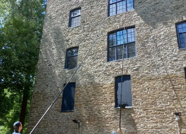 Two men cleaning windows of a large stone building.
