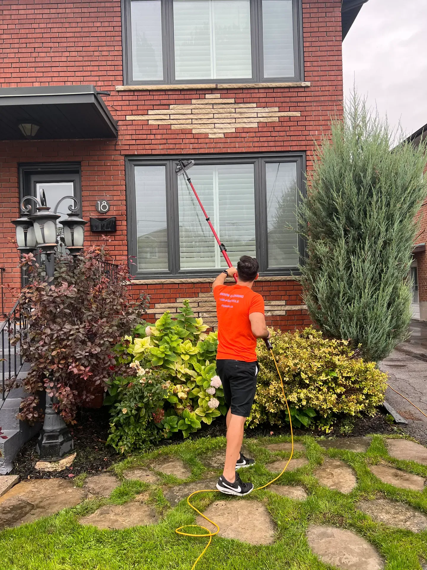 Man cleaning window with long-handled brush at brick house.