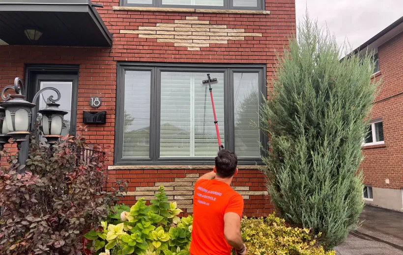 Man cleaning windows with long brush at brick house.