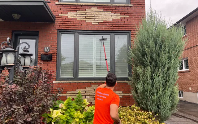 Man cleaning windows with long brush at brick house.