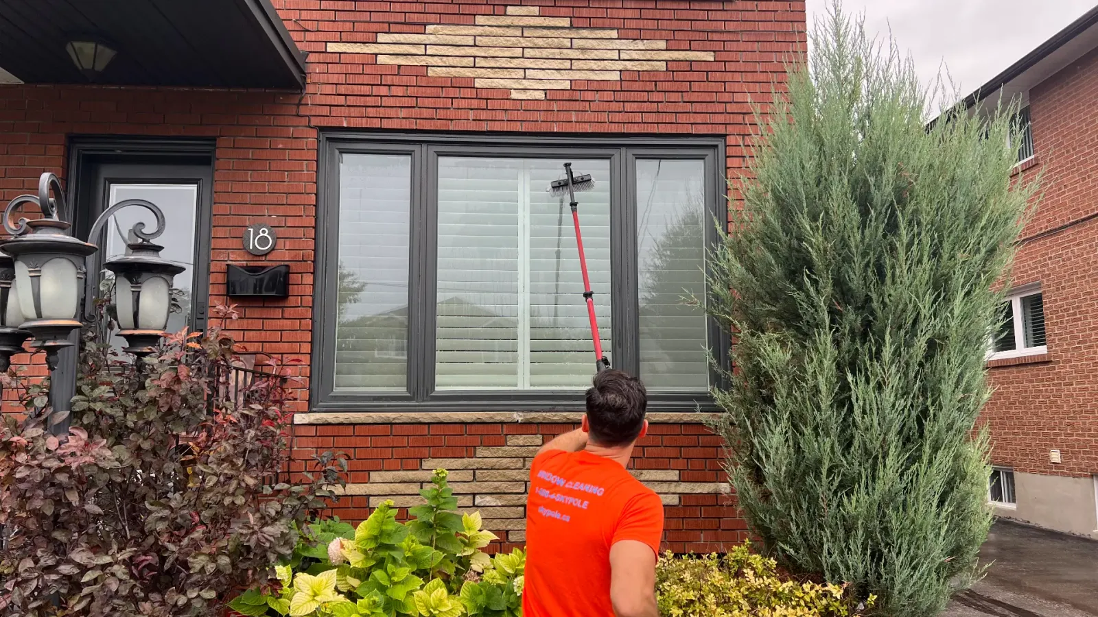 Man cleaning windows with long brush at brick house.