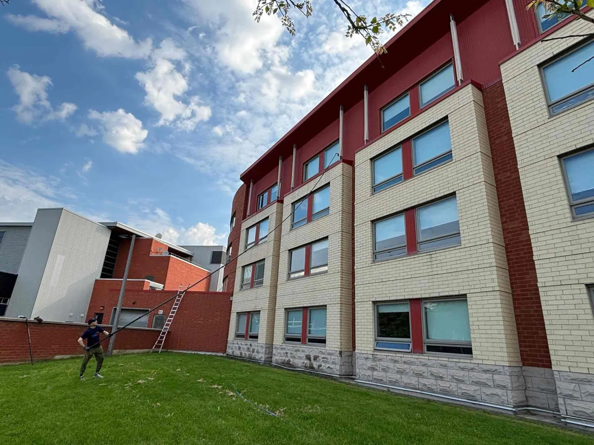 Man carrying ladder near modern brick building with windows