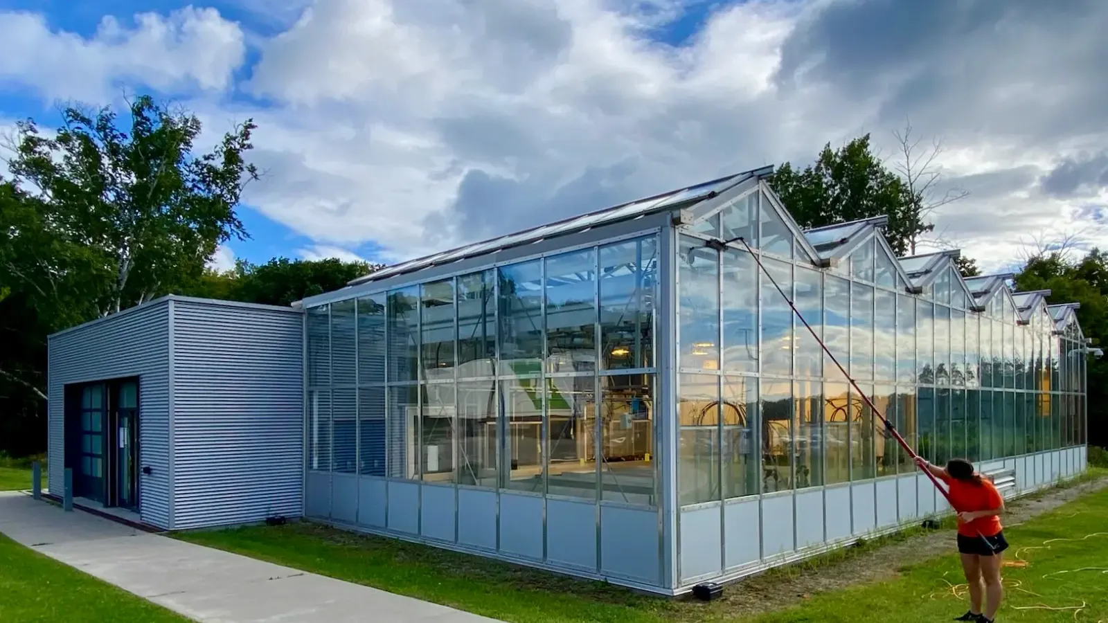 Person cleaning modern glasshouse exterior with hose.