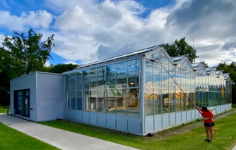 Person cleaning modern glasshouse exterior with hose.