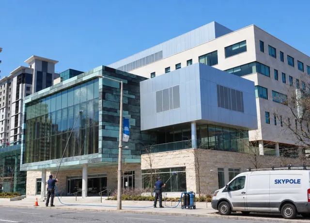 SKYPOLE crew using water-fed poles to clean exterior windows at McMaster University Health Sciences Campus in Hamilton, with a branded service van nearby.